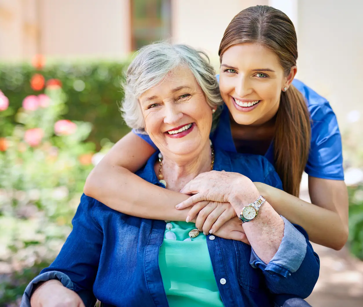 Smiling woman hugging elderly woman outdoors.